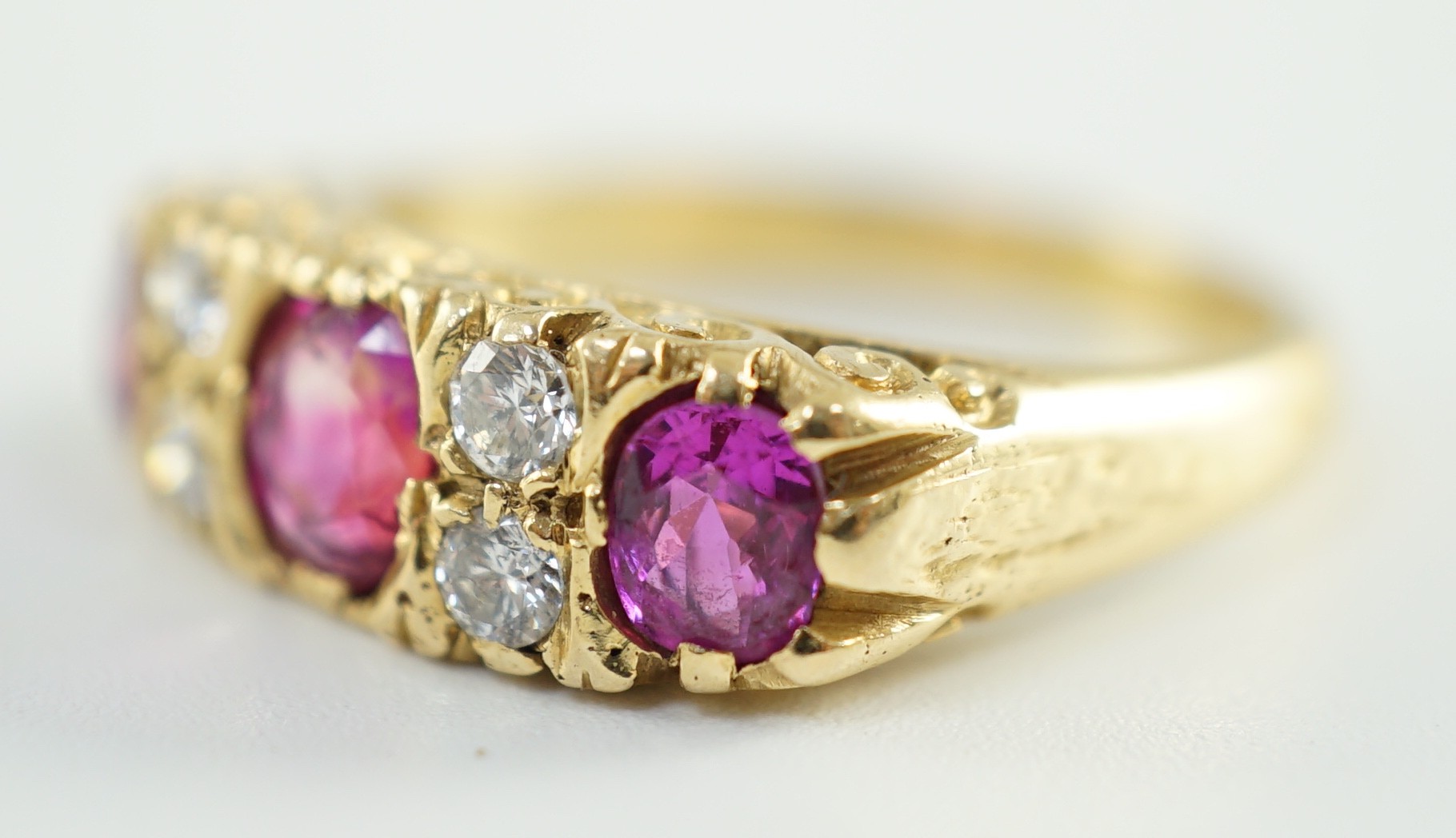 An early to mid 20th century 18ct gold, single stone oval cut ruby, two stone pink sapphire and four stone round cut diamond set half hoop ring